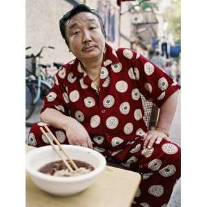  Man in Silk Pajamas Eats a Bowl of Noodles on the Street 